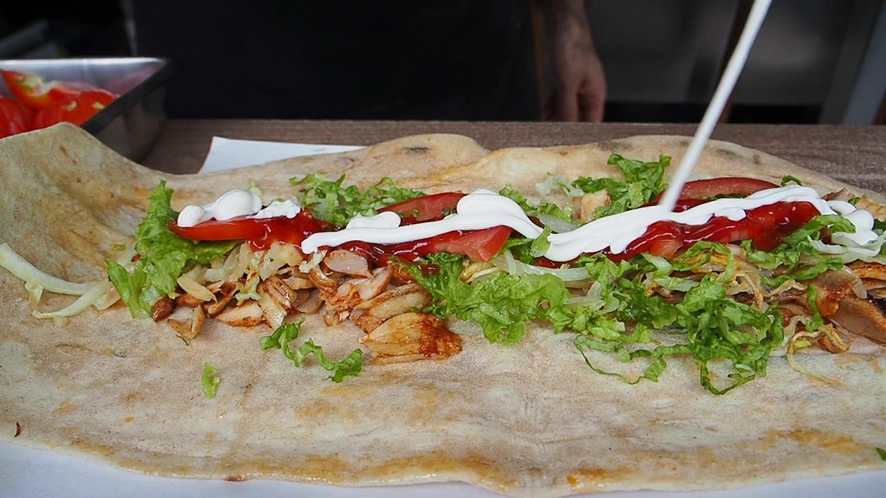 Chef che aggiunge ketchup e maionese a un wrap di kebab di pollo.