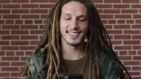 portrait of attractive mixed race man with dreadlocks smiling happy using smartphone