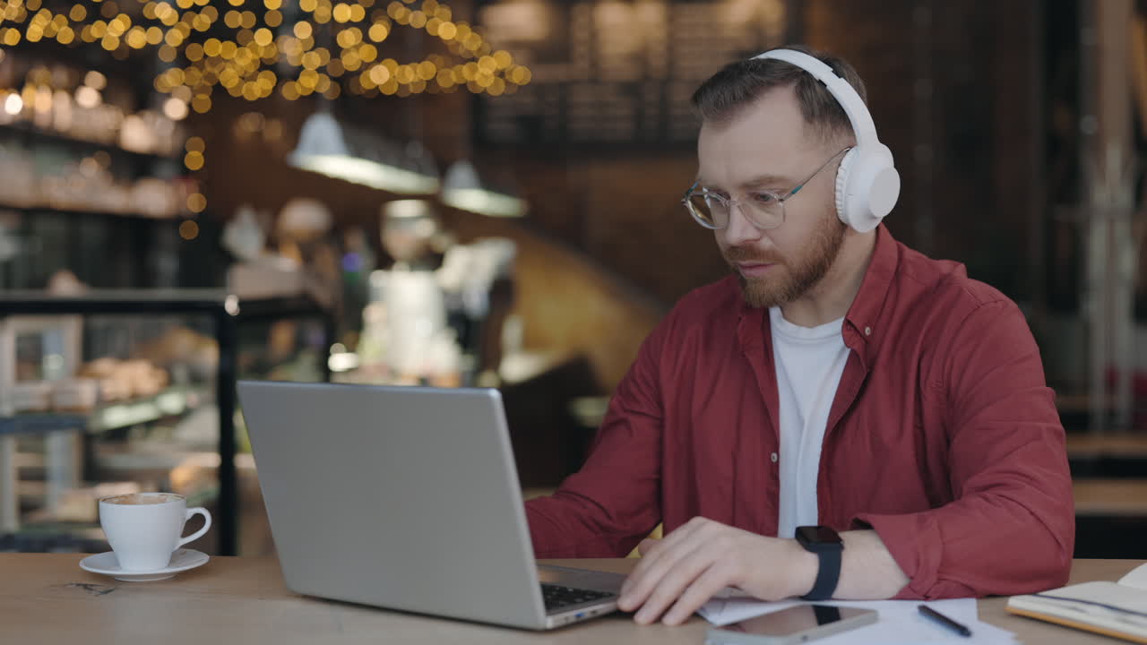 Man Working on Laptop in Cafe with Headphones
