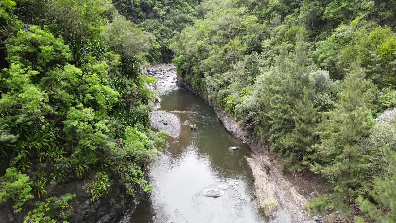 Drone footage of a river in a green canyon with two people in the water in the Cirque of Mafate on the Reunion island