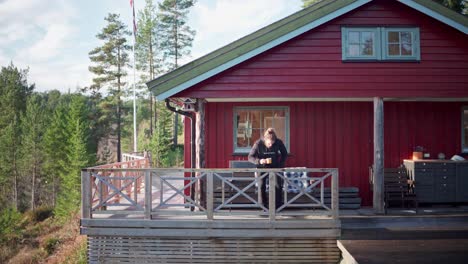 man holding a cup of coffee sits on the chair in the cabin on a sunny day