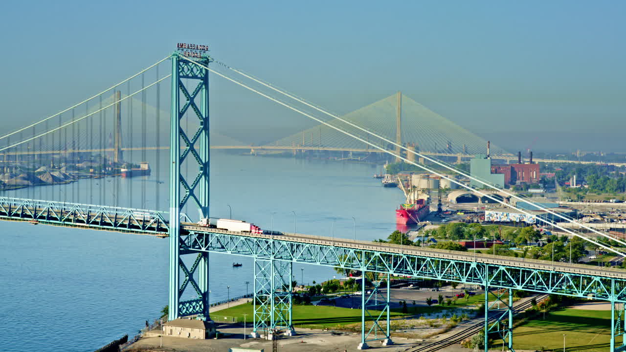 Drone shot rising above Detroit River, framing the skyline with a freighter moving below