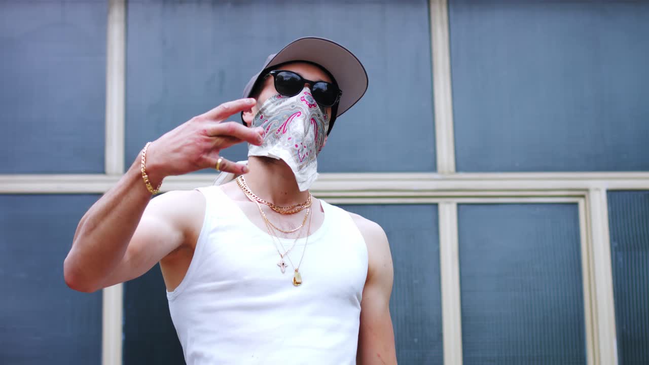 목에 금목걸이를 두르고 얼굴에 스카프를 두른 성인 남자가 손으로 w를 만든다