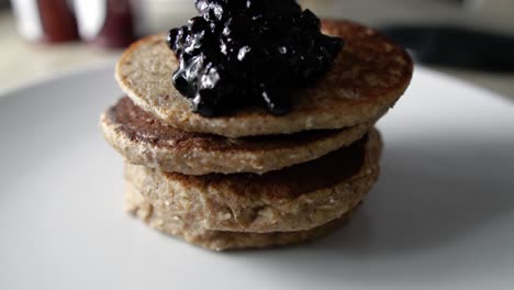 placing cooked blueberry sauce on top of four stacked pancakes, slow motion