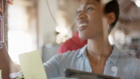 Happy-african-american-colleagues-taking-notes-on-glass-wall-and-discussing-work,-slow-motion