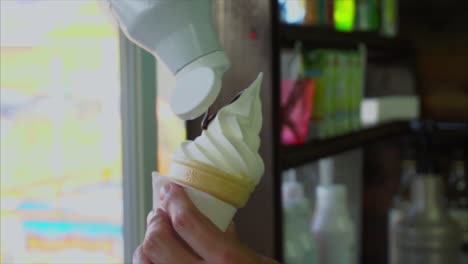 person serving ice cream cone with chocolate topping