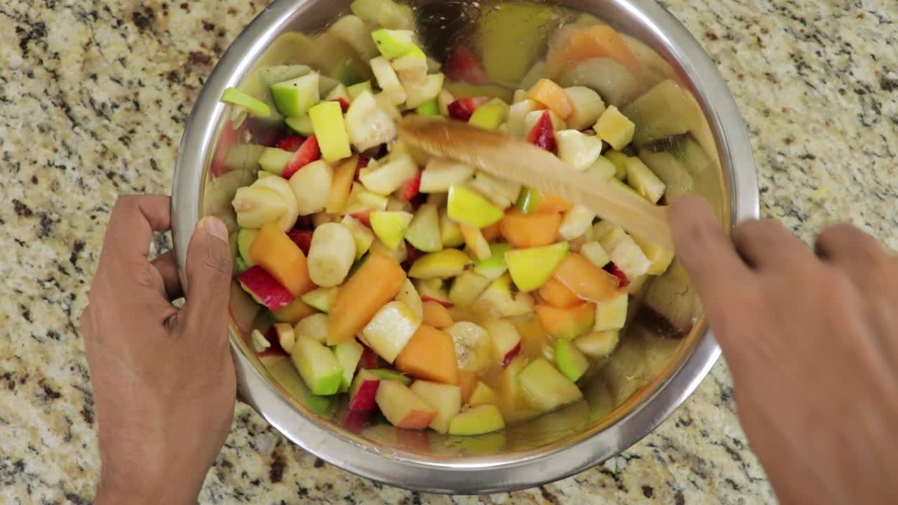 Pezzi di frutta succosi mescolati in una ciotola con un cucchiaio di legno, vista dall'alto