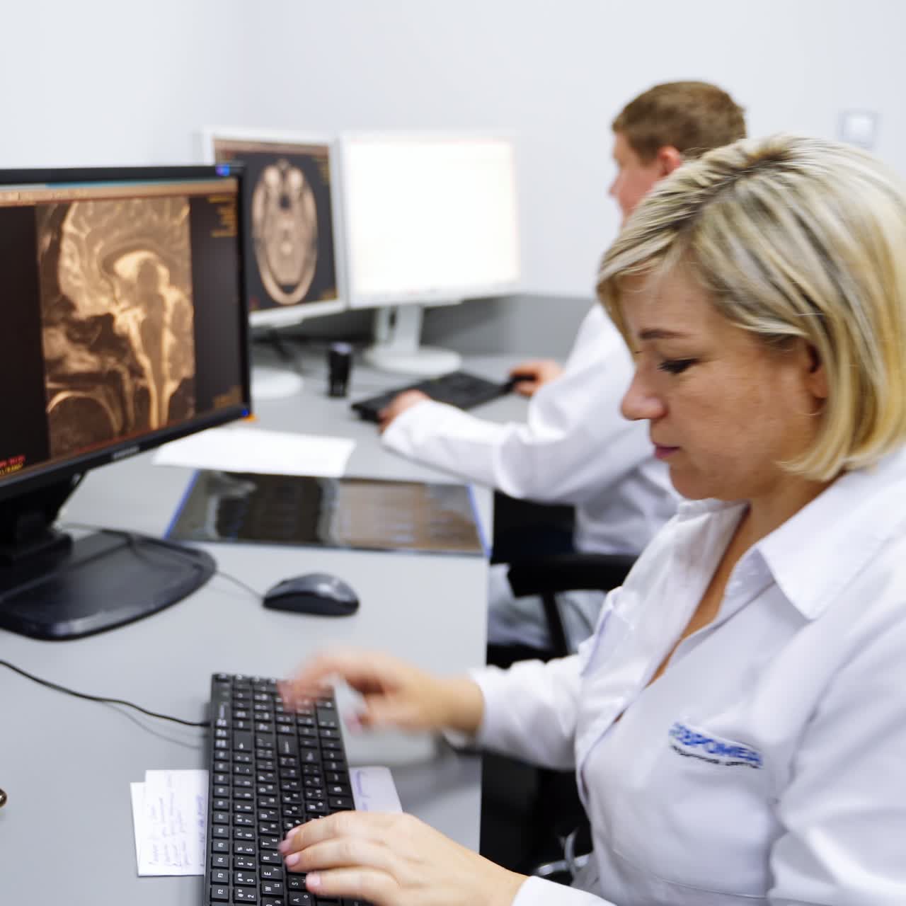 Lab technicians working at computers looking through the MRI scans. Female expert starting to describe the images