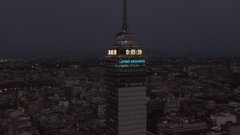 Backwards-reveal-of-cityscape-around-Torre-Latinoamericana-tall-building-at-night.-Large-digital-neon-clock.-Mexico-City,-Mexico.