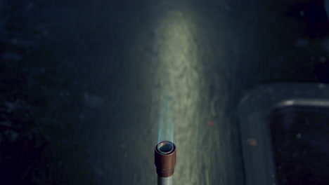 close up of bunsen burner tip on a black lab bench burning with blue flame