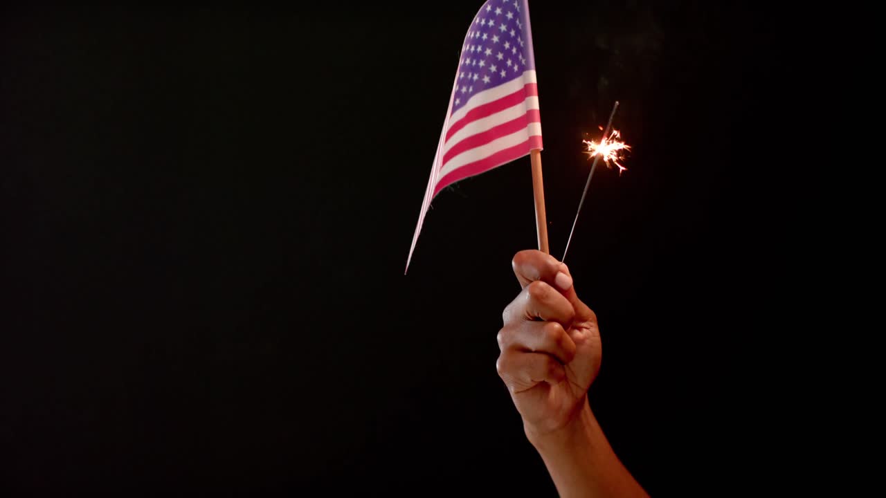cerca de la mano sosteniendo la bandera nacional de los ee.uu. y chispas en fondo negro