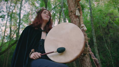 Niña-Druida-En-Un-Bosque-Tocando-Su-Tambor-Chamánico-Plano-Medio-De-ángulo-Bajo