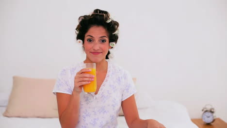 mujer alegre con rizos de cabello disfrutando de jugo de naranja