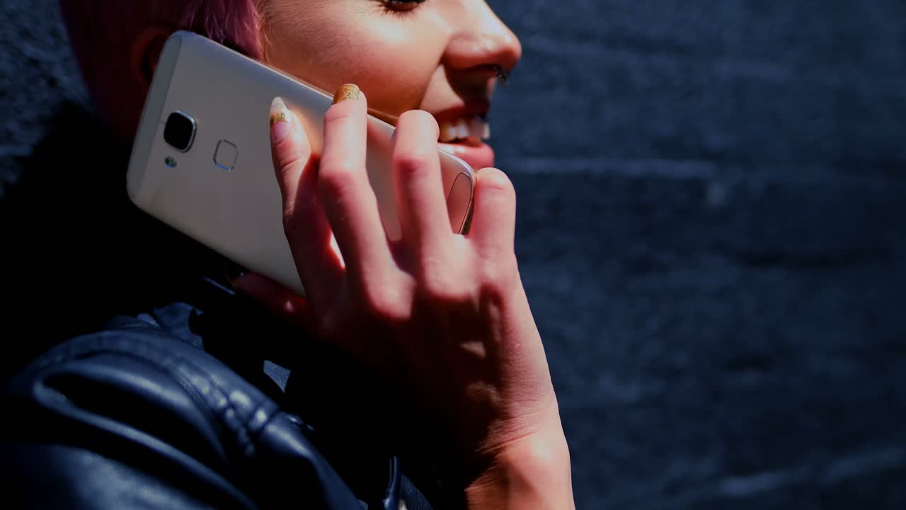 장미 머리카락의 여성이 골목 4k에서 휴대 전화로 이야기하고 있습니다.