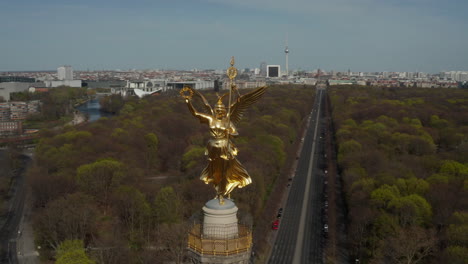 AERIAL:-Close-Up-Circling-around-Berlin-Victory-Column-Golden-Statue-Victoria-in-Beautiful-Sunlight-and-Berlin,-Germany-Cityscape-Skyline-in-Background