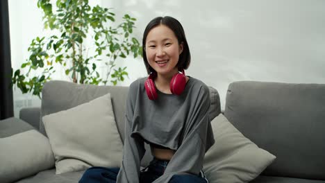 Portrait-of-gentle-asian-lady-wearing-wireless-headphones,-sitting-on-couch