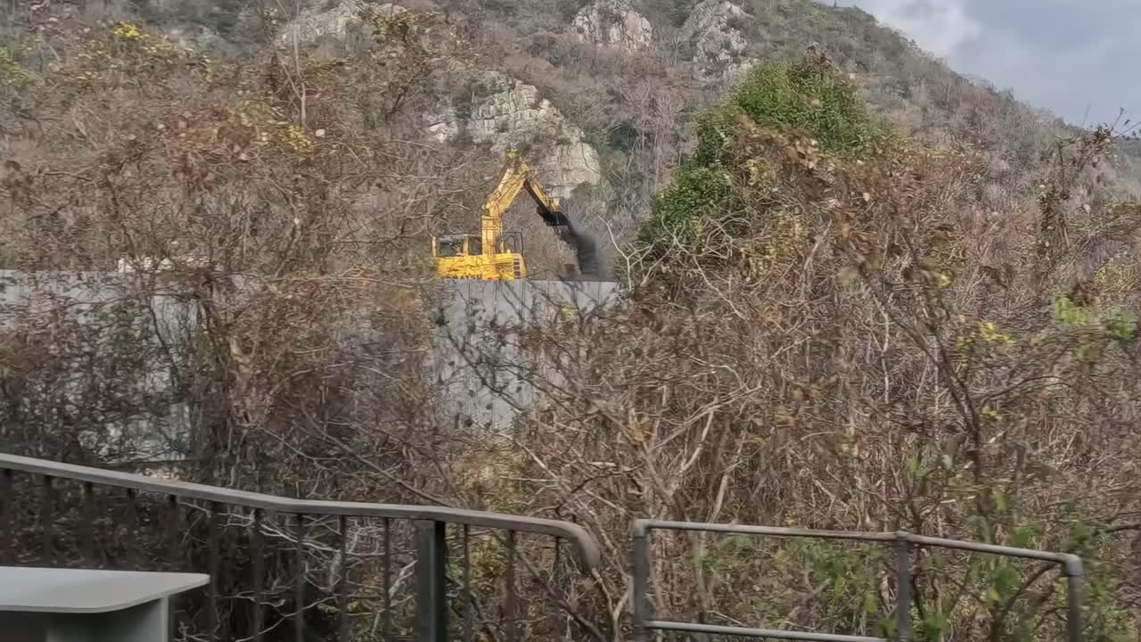 A scenic view of mountains, construction sites, and diverse vegetation captured from a moving perspective.