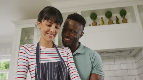 una pareja feliz y diversa con un delantal azul abrazándose y cocinando en la cocina