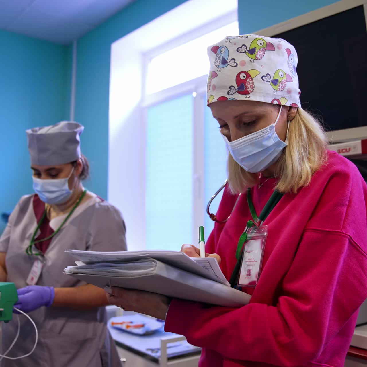 Female anesthesiologist taking notes in the surgery room. Nurse at backdrop arranging drop counter