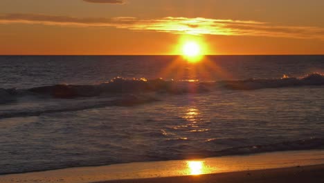 Sol-Saliendo-Sobre-Las-Olas-En-La-Playa,-Amanecer-Costero-En-Cámara-Lenta,-Plano-General,-Mar-Mediterráneo,-España