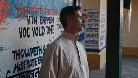 mature man in traditional indian clothing stands contemplatively, observing multilingual signs painted on a wall, possibly reflecting on cultural diversity and communication