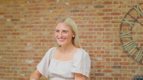 young woman standing by wooden staircase at home talking and laughing with person off camera