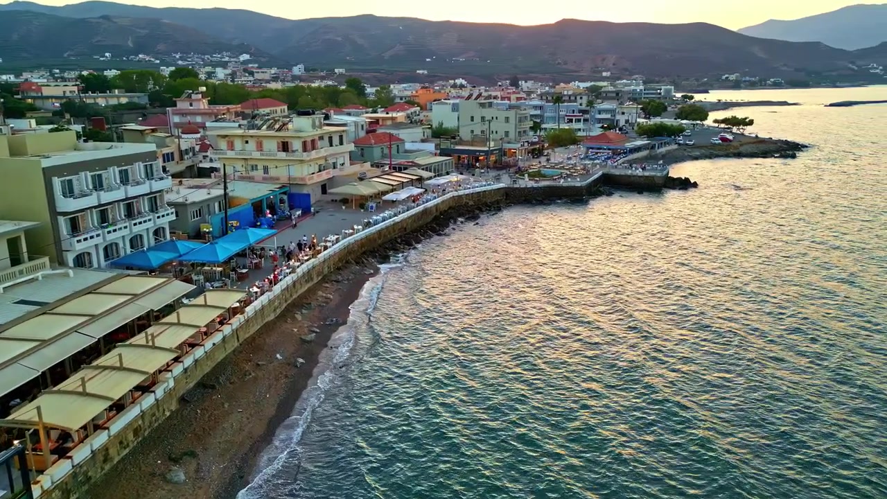 Gün batımı ışığında, sakin sulara ve binalara sahip huzurlu bir sahil kasabası.
