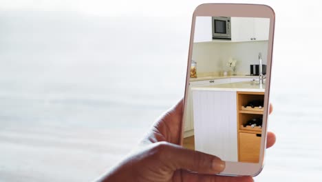persona que sostiene un teléfono inteligente con interiores de cocina modernos mostrados en la pantalla