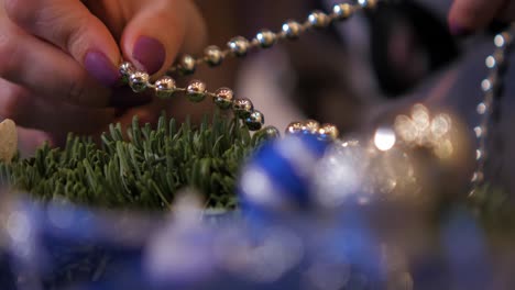 woman making a fir advent wreath for christmas eve and decorating it with silver pearls, diy craft decoration, winter traditions, seasonal holidays, hands close up handheld shot