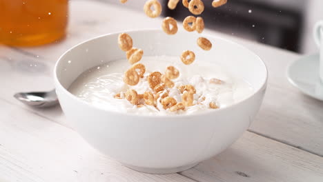 cereales de grano entero en forma de círculo que caen en cámara lenta en un tazón blanco de leche en una mesa de la cocina
