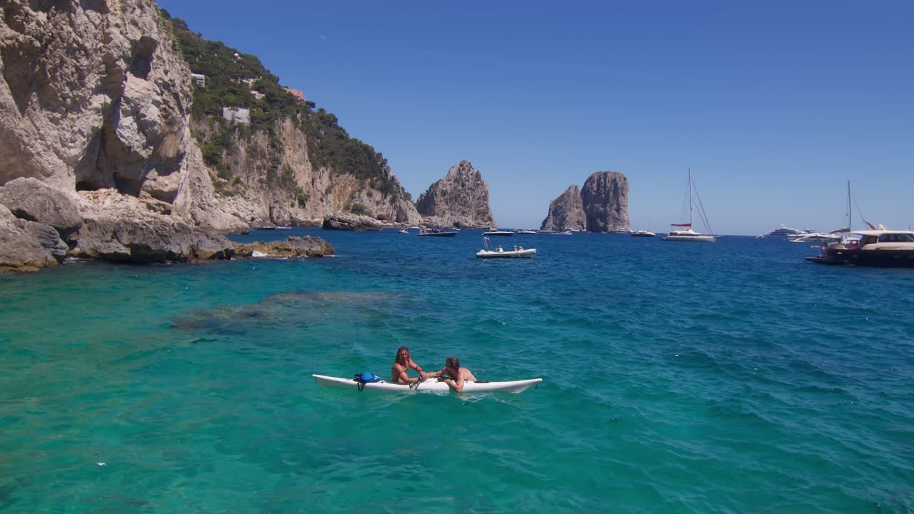 Two friends relax in a kayak, chatting against the stunning backdrop of Capri's Faraglioni