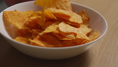 close up of person at home pouring tortilla or corn chips from packet into bowl on table