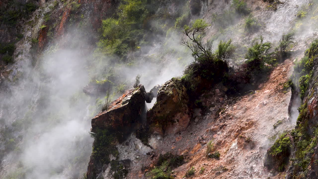 primer plano de vapor tóxico que se eleva a lo largo de las montañas rocosas con plantas durante el día soleado - lago del cráter geotérmico en nueva zelanda