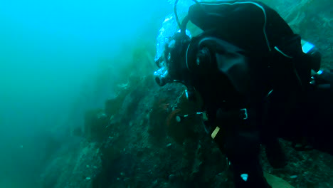 slow motion shot of diver in full equipment swimming underwater, breathing out, bubble appearing next to diving mask