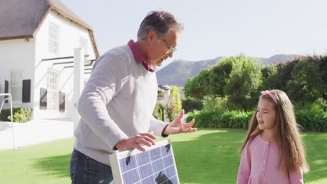 Video-Eines-Glücklichen-Kaukasischen-Großvaters,-Der-Seiner-Enkelin-Im-Sonnigen-Garten-Das-Solarpanel-Erklärt