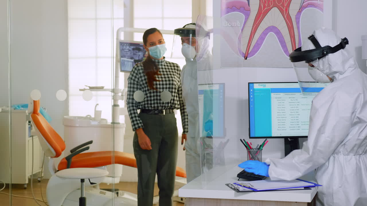 médico con traje de protección invitando al siguiente paciente a la sala dental