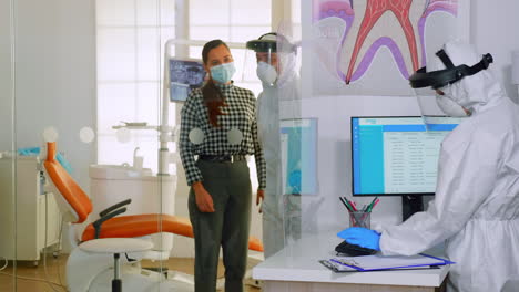 Doctor-with-protection-suit-inviting-next-patient-in-dental-room