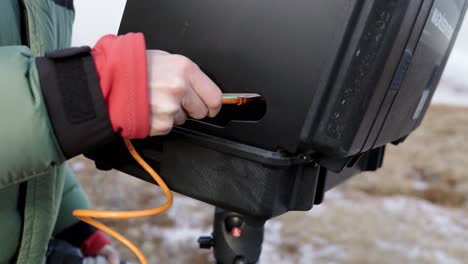 outdoor photographer plugging in orange usb-c cable into laptop on stand