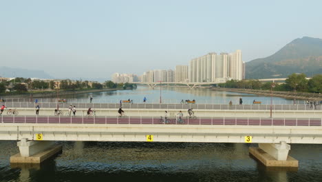 Stunning-drone-panning-shot-of-cyclists-riding-over-a-bridge-at-sunset