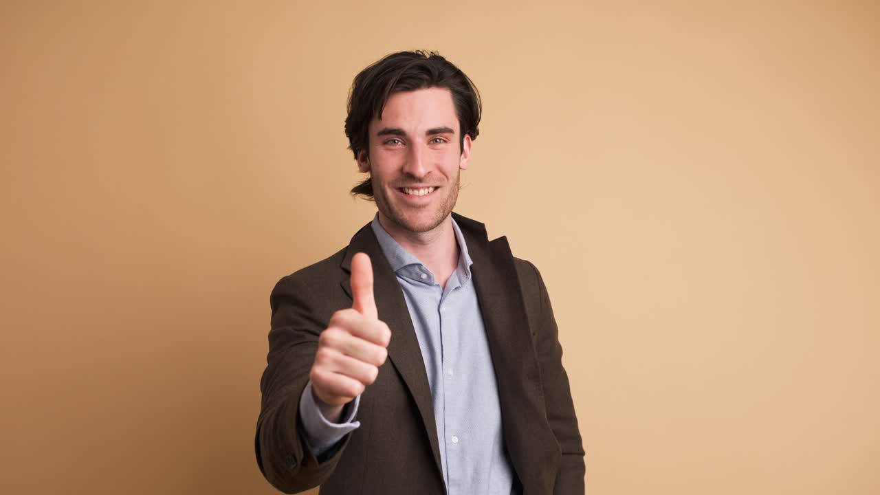 Happy businessman showing thumbs up in brown studio