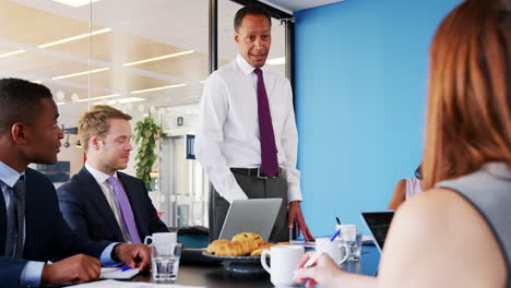 manager stands addressing colleagues at a business meeting