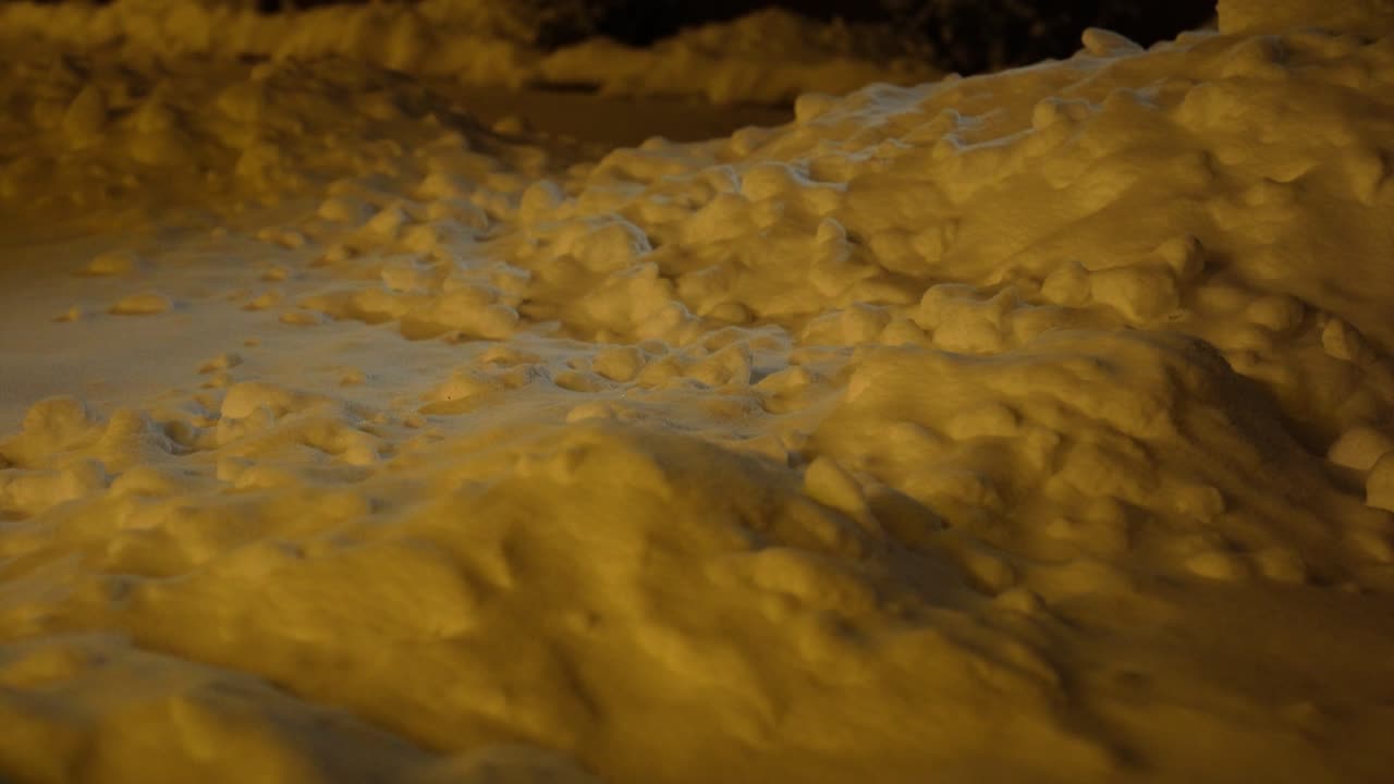 Cumuli di neve che creano forme irregolari, illuminati da una luce artificiale calda in un ambiente invernale