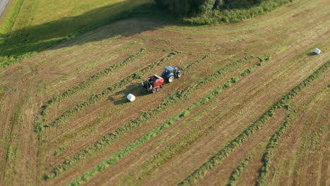 El-Tractor-Moviéndose-Lentamente,-Recogiendo-Hierba-Y-Empaquetándola-En-Rollos-De-Plástico-Blanco-Y-Limpio