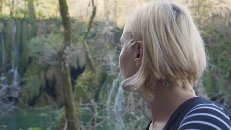 beautiful girl with short blond hair enjoying the natural beauty of the forest and the waterfall