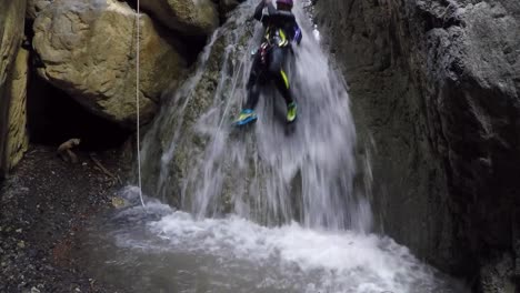female adventurer in wetsuit slides down rope in canyon waterfall