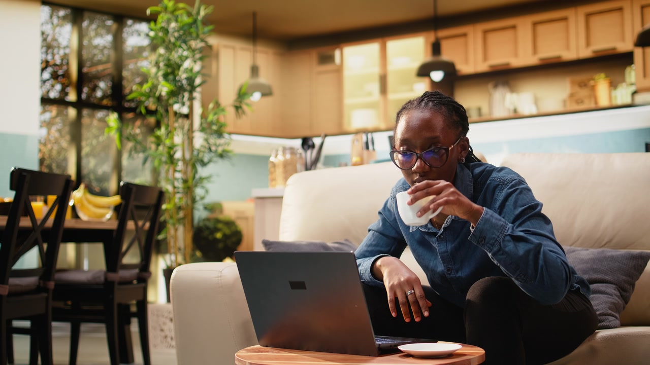 Young woman solving online work and tasks with laptop at kitchen table