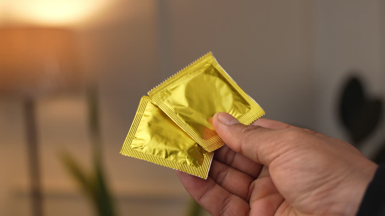 Mostrando embalagens de preservativos sendo seguradas em um dedo