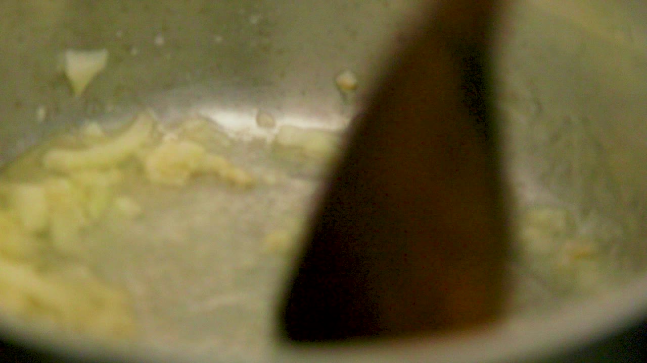 Wooden spoon mixes onion and olive oil in a pan