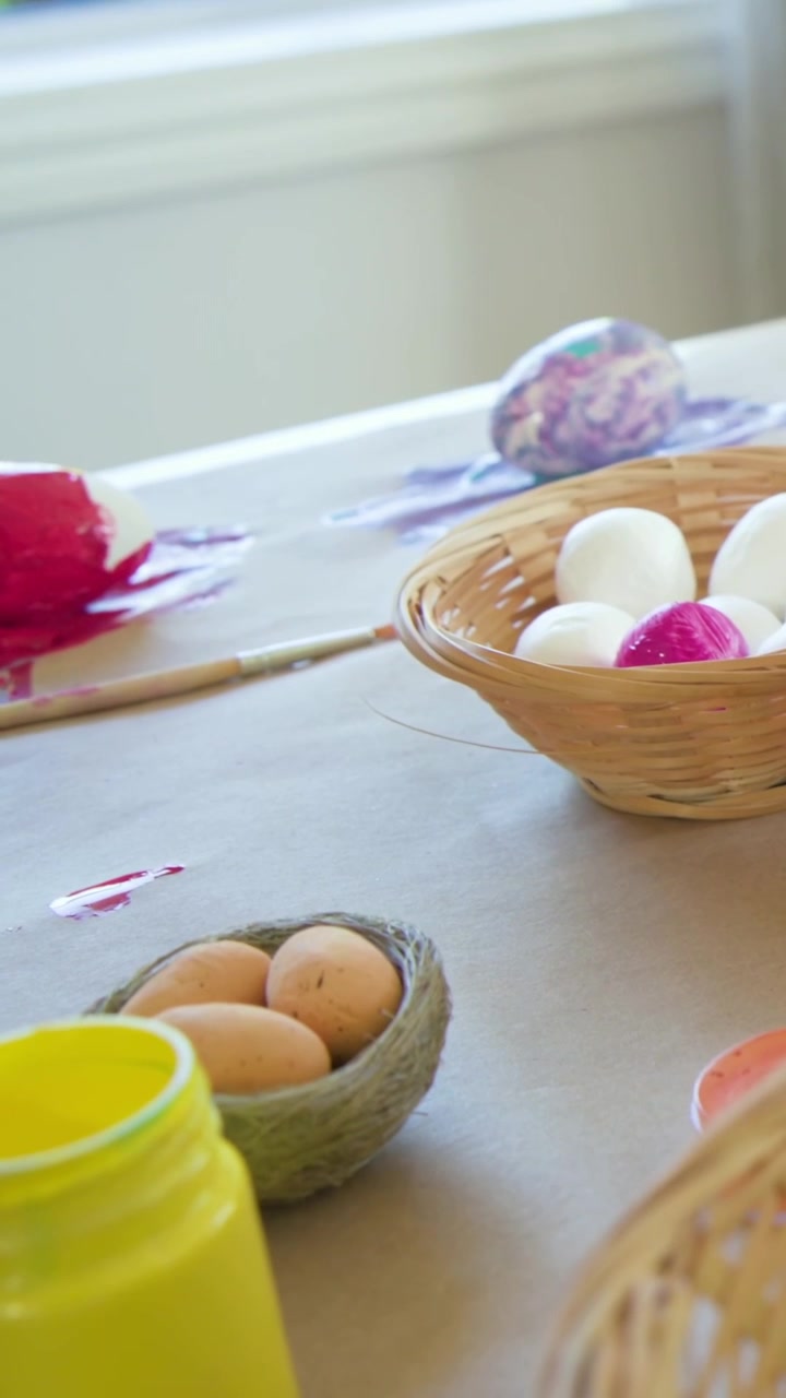Vertical video: Panning camera revealing craft table at home, showing yellow paint jar and eggs