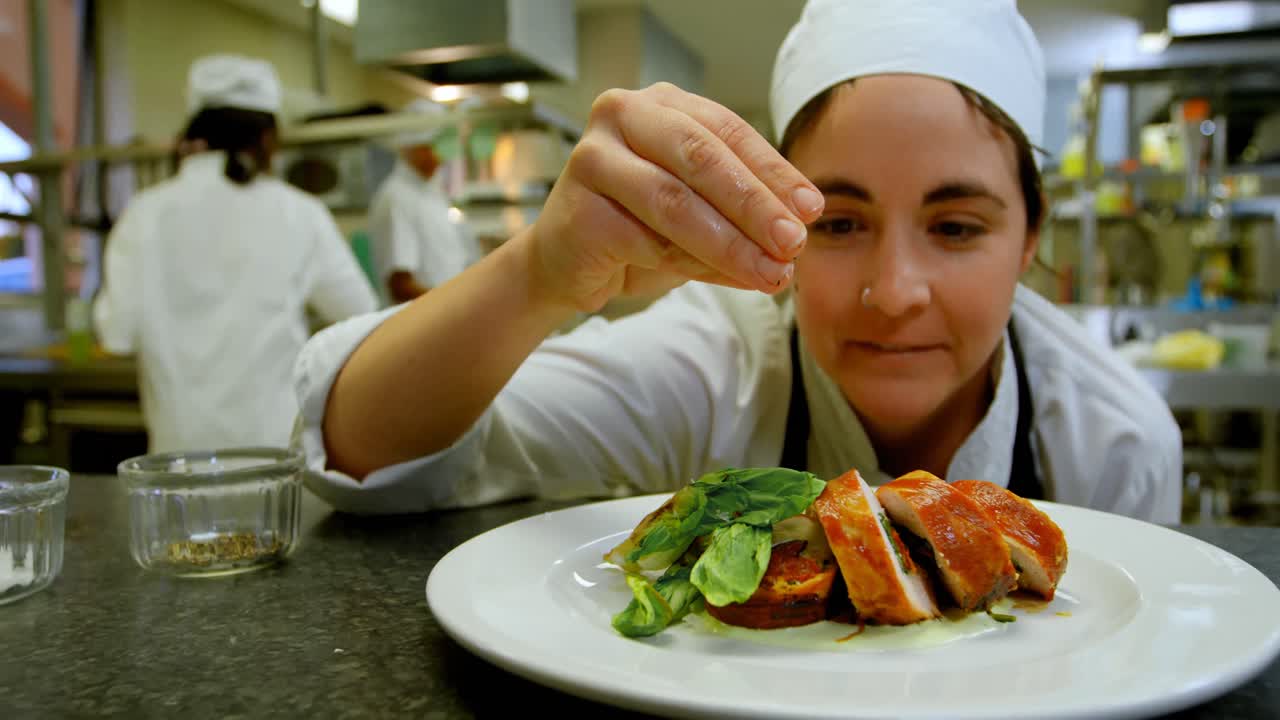 chef femenino rociando sal en el plato en la cocina 4k
